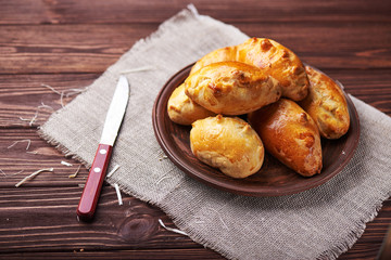 Delicious rustic pastries filled with meat and vegetables on a ceramic plate with wooden knife on a wooden background.