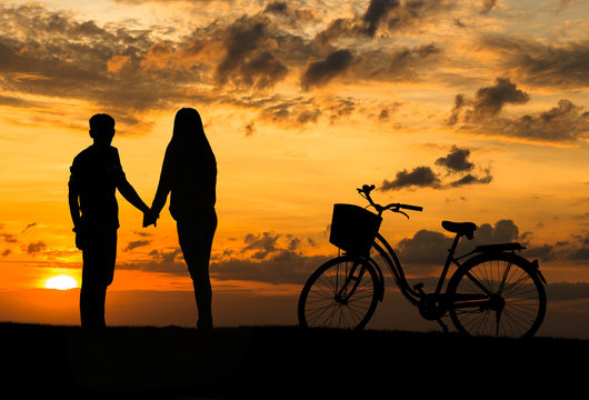 Silhouette of sweet couple in love happy time and bicycle in bea