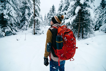 Man with backpack and thermos  is hiking in snowy winter forest