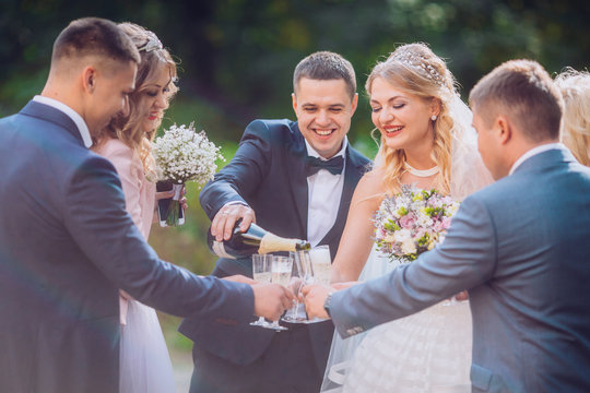 Bride and groom with happy groomsmen and bridesmaids having fun and popping champagne, luxury wedding celebration, hilarious moment. Newlyweds fun with friends.