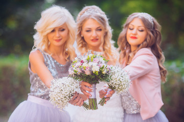 Bride with bridesmaids in the park with flowers on the wedding day