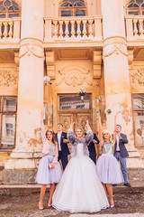Bride with bridesmaids throw bouquets of flowers and groomsmen try to catch it. Friends near old castle with columns