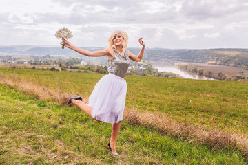 Pretty young girl in a field with flowers in hand, a bridesmaid in a silver dress jumping