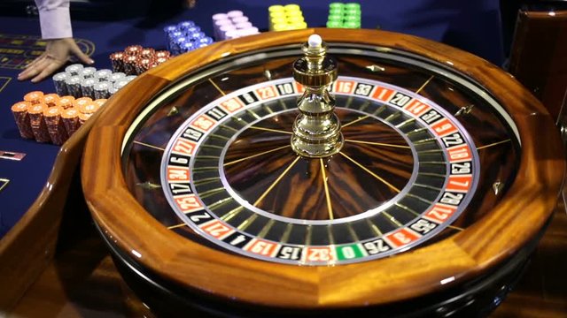 Roulette table in casino. Ball in the rotating gambling machine. Wooden roulette wheel. Casino croupier releases roulette white ball.