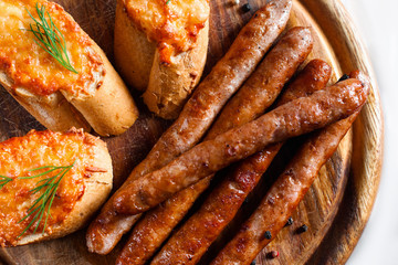 Tasty bavarian wurst with toasts flat lay. Top view on wooden catering platter served with grilled sausages and three canapes. German cuisine, beer snack, junk food concept