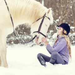 Young teenage girl holding hands to white horse in winter park