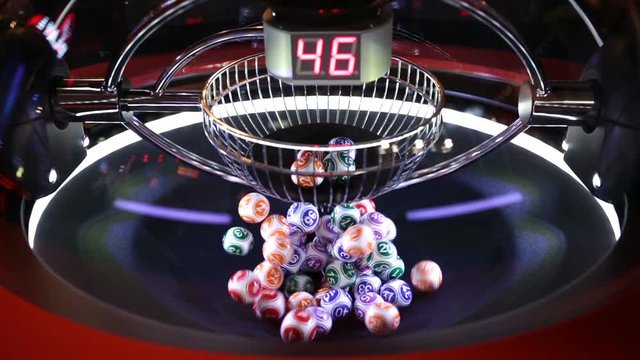 Colourful lottery balls in a rotating bingo machine. Different numbers on a red digital monitor.