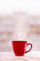 Steaming hot tea cup with heart shaped smoke on rainy background