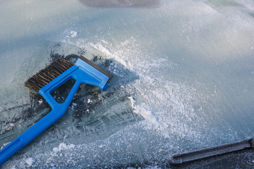ice scraper cleaning a frozen windshield of a car, winter traffic background