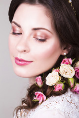 Fototapeta premium Beautiful brunette bride smiling with natural make up and flowers roses in her hairstyle and looking sideways