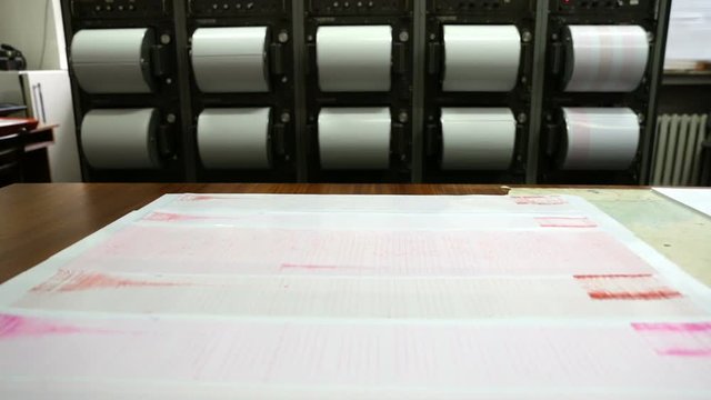 Seismograph records an earthquake on the sheet of measuring paper. Seismological device for measuring earthquakes. Seismograph machine needle drawing a red line on graph paper measuring activity.