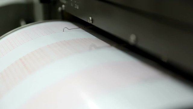 Seismograph records an earthquake on the sheet of measuring paper. Seismological device for measuring earthquakes. Seismograph machine needle drawing a red line on graph paper measuring activity.
