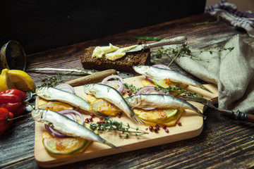 Fresh fish with aromatic herbs, spices, salt, onion rings, bread, bottles with olive oil and balsamic vinegar,perch on cracker, on dark vintage background, top view, healthy food