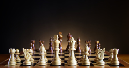 chessboard with wooden figures, white figures on foreground, chess with a dark color gradient background 