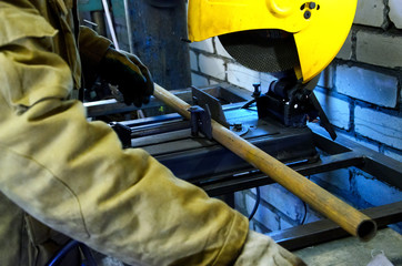 Worker holds hands the metall pipe to cut it on the machine. Against the background of white bricks