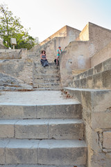 Girl and woman sit on old yellow stone staircase of limestone in the Santa Barbara castle, Alicante, Spain