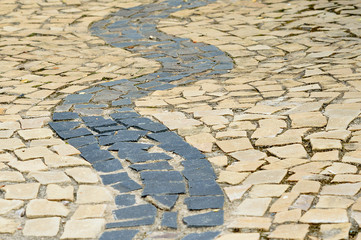 Waves mosaic made with black and beige rocks on a sidewalk