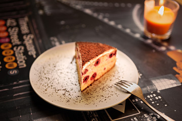 Piece of cherry cake and candle on a dark table. Romantic dessert in cafe in evening. 