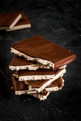 Stack of pieces of chocolate filled with white nougat on a dark stone table, copy space