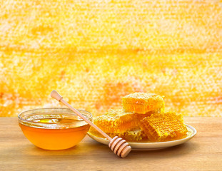 Honey in glass bowl, wooden honey dipper and honeycombs with honey on wooden table on background honeycombs with full cells of honey.
