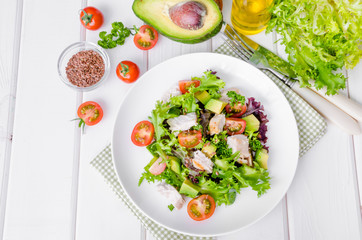 Fresh salad with chicken, avocado, tomatoes and flax seeds on a plate on white wooden background. Healthy food.