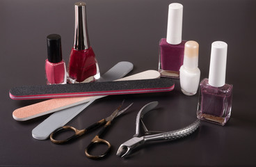 scissors, nail files and clippers manicure with polish bottles on a dark background