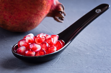 pomegranate seeds in a ceramic spoon and a sprig of rosemary on a dark surface