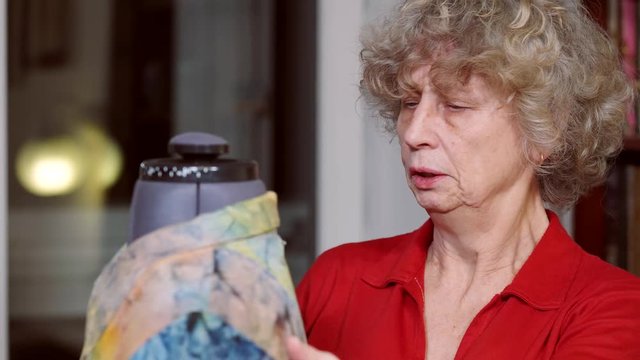 Senior woman making a dress on a mannequin. In the room, even light. Woman clothes red