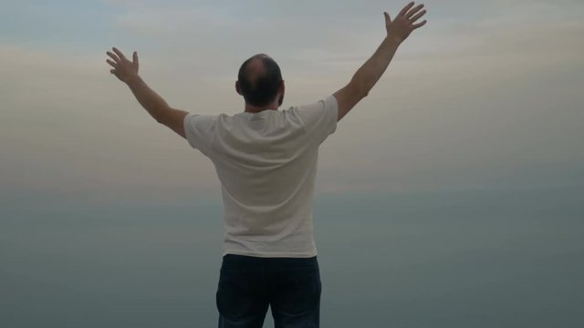 Man worshiping god, standing on hill and raising hands to sky. Beautiful landscape of Dead Sea on background.