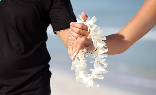 Couple hands holding Flower lei garland of white plumeria.