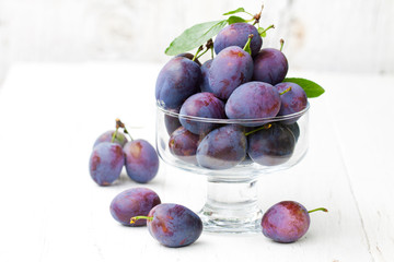 Fresh  ripe plums in a glass bowl on white background
