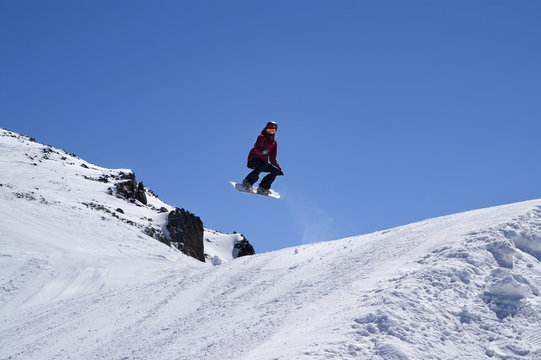 Snowboarder jumping in terrain park at ski resort on sun winter