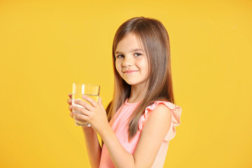 Attractive little girl holding glass of water on yellow background