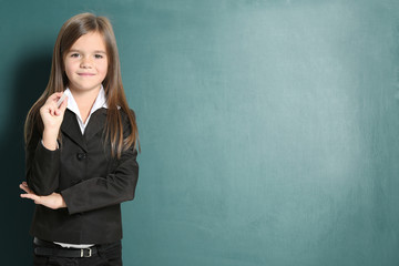 Cute little girl with piece of chalk standing on green blackboard background
