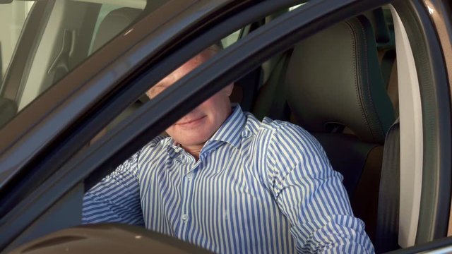 Caucasian mature man sitting into the car at the dealership. Middle aged client showing thumb up through the window. Attractive male customer closing car door