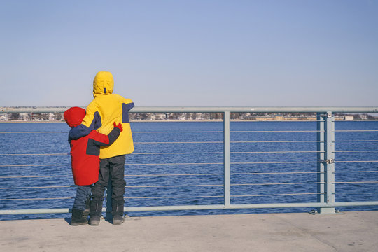 children stand in an embrace on the waterfront. two kids hugging looking at the sea. empty space for your text