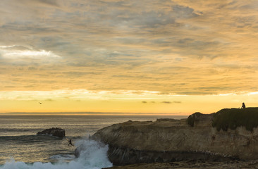 Surfer jumps off cliff into ocean at sunset in California