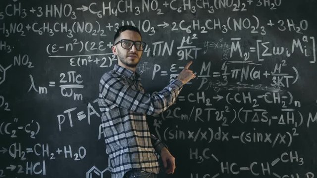 Young scientist man write chock in chemical and mathematical equations wall room interior