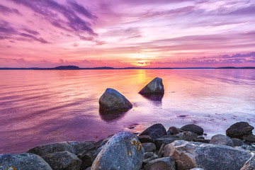 Picturesque sea sunset landscape with large stones at foreground. Violet toning of beautiful...