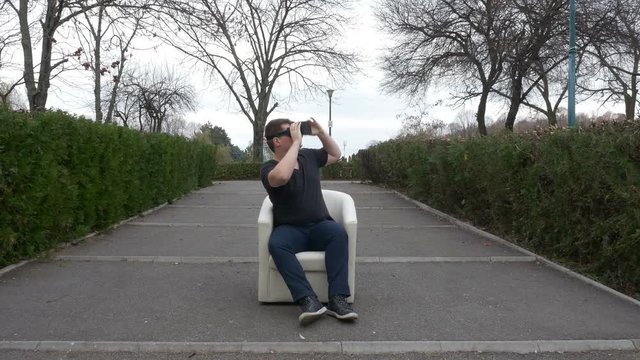 Guy using VR glasses making specific gestures and looking around in the park