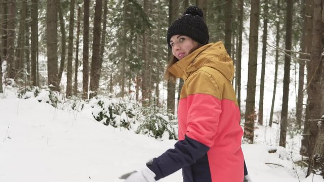 Happy smiling woman in winter cloths outdoors in forest comes up smiling and waves with her hand