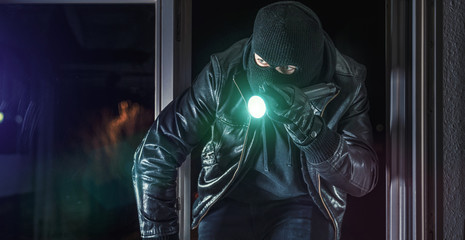 Einbrecher mit Brecheisen und Taschenlampe im Fenster eines Hauses