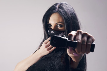 Beautiful brunette woman with a pistol pointing to camera, wearing a bandana as a thief, looking menacing. Over a grey background.