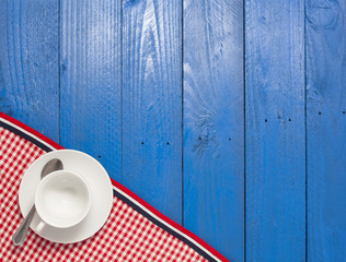 empty white coffee cup with red  tablecloth on blue wooden 