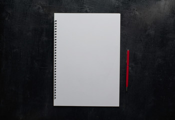 Wooden black office desk table with notebook and red pen . Blank notebook page for input the text in the middle. Top view