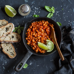 Braised beans in tomato sauce in a cast iron pan and homemade bread on wooden cutting board. Vegetarian food concept