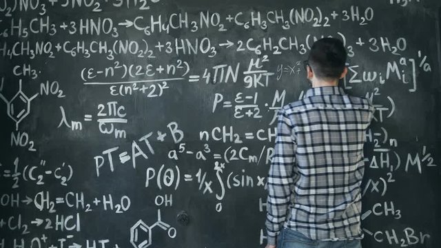 Young scientist man write chock in chemical and mathematical equations wall room interior