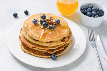 Stack of pancakes with fresh blueberries, walnuts and honey on white plate. Healthy breakfast food. Closeup side view