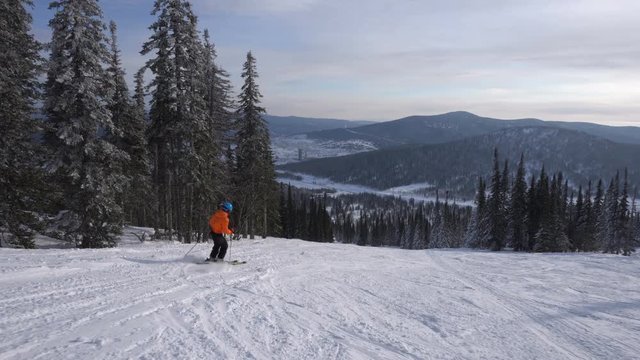 Skier is riding down from the peak of mountain to snow-covered valley
