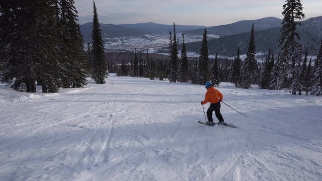 Woman skier is riding down slowly from the peak of mountain to snow-covered valley